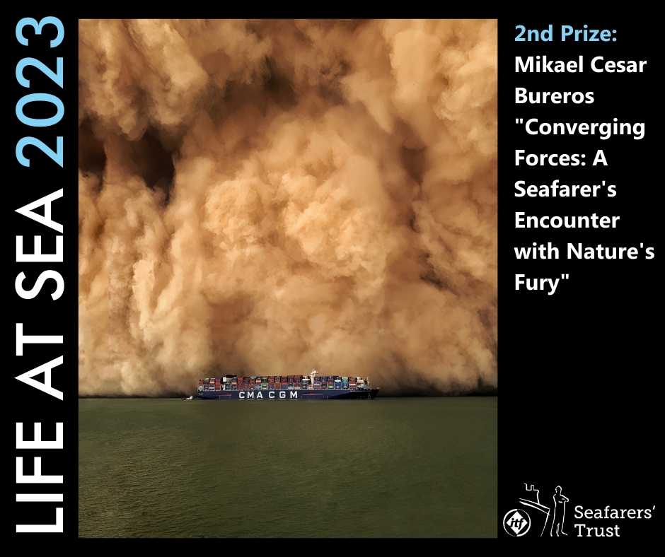 A graphic showing the 2nd Prize photo on a black background with text reading Life At Sea 2023 2nd Prize Winner Mikael Cesar Bureros "Converging Forces: A Seafarer's Encounter with Nature's Fury". The picture is of a container ship at sea, dwarfed by the massive sandstorm about to engulf it which fills the whole picture behind the ship. 